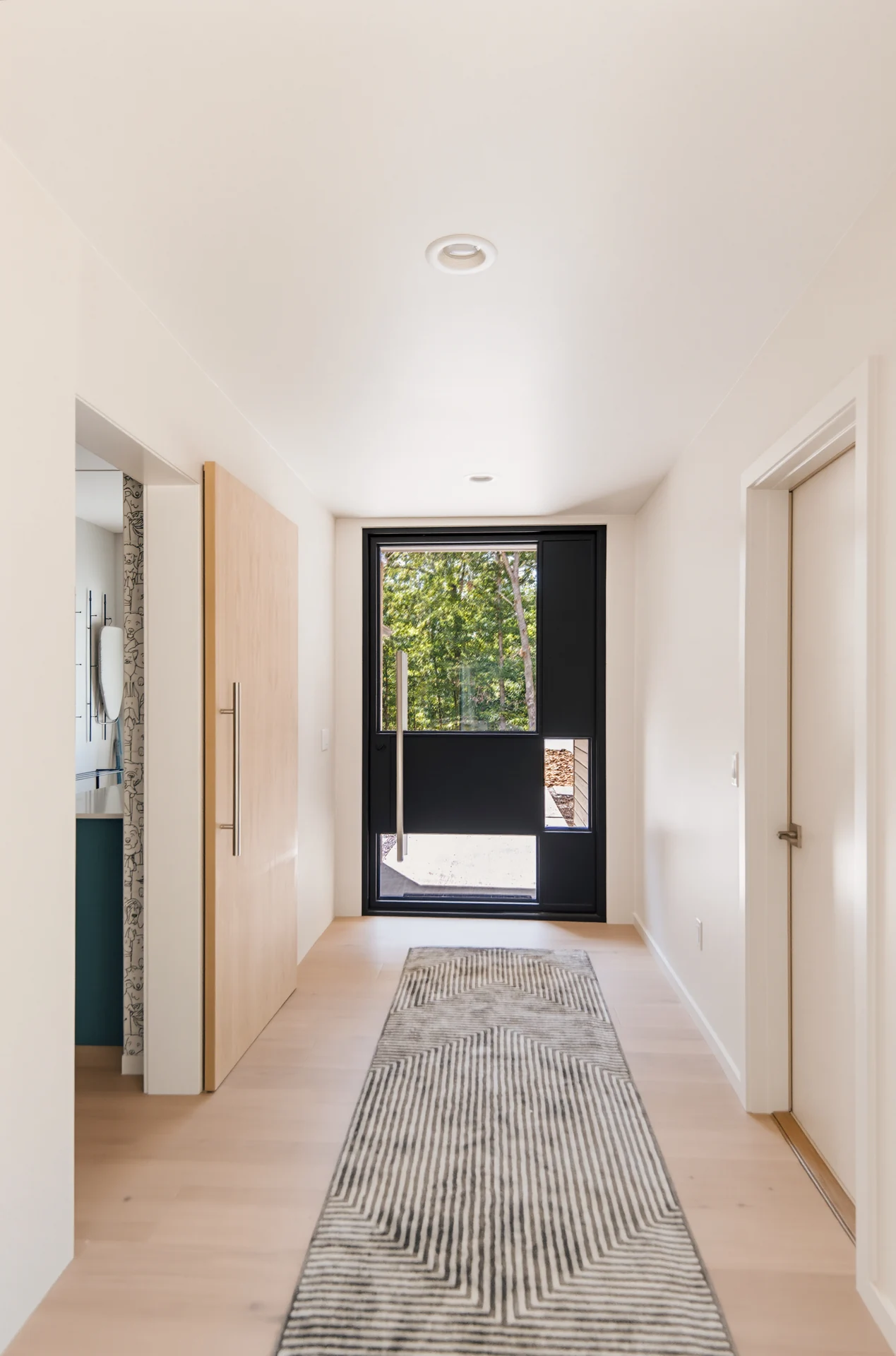 Hallway leading to a dark-framed glazed entry door