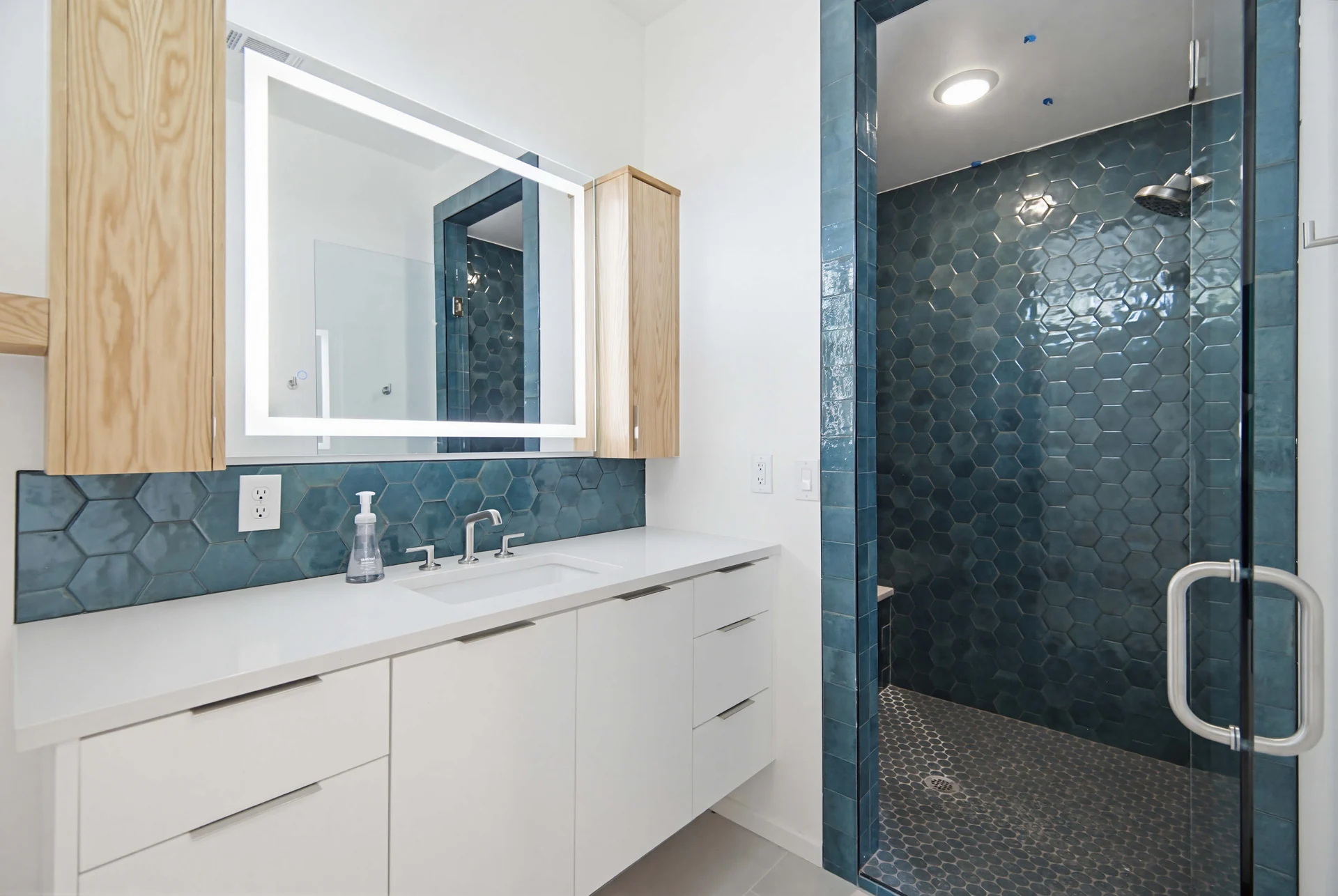 Bathroom vanity beside a blue-green tiled shower